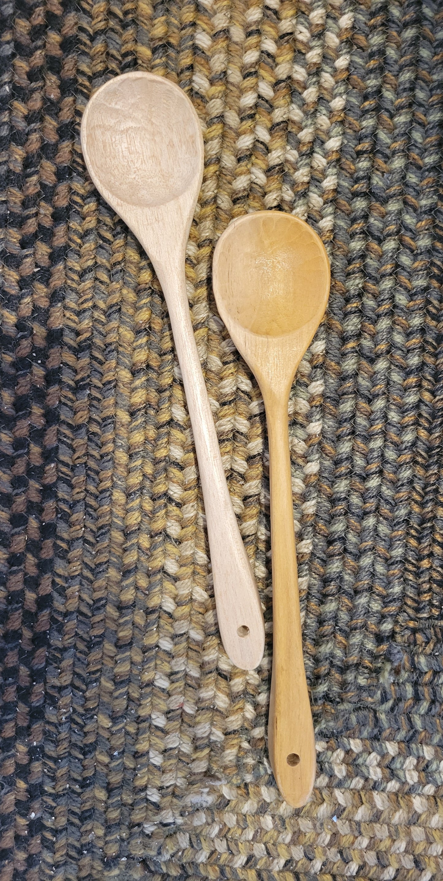 One light colored and one darker stained wooden spoon laying on a braided rug