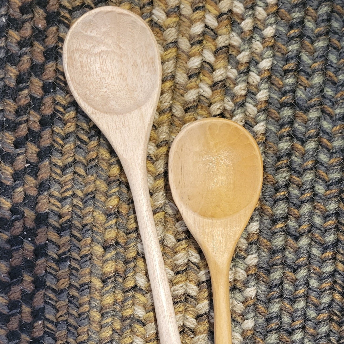 One light colored and one darker stained wooden spoon laying on a braided rug